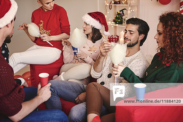 Junge Frauen und Männer essen auf der Weihnachtsfeier Zuckerwatte auf dem Sofa