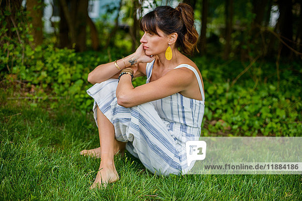 Mittlere erwachsene Frau sitzt im Garten im Schneidersitz