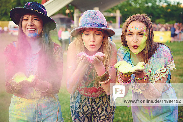 Drei junge Frauen blasen auf dem Festival farbiges Kreidepulver