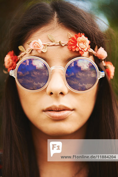 Porträt einer jungen Hippiefrau mit Blumenstirnband und Sonnenbrille beim Festival