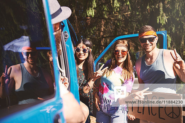Young boho hitchhikers with peace sign by recreational van
