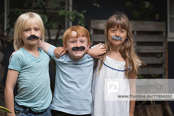 Children wearing fake mustaches looking at camera smiling