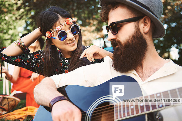 Young boho couple playing acoustic guitar at festival