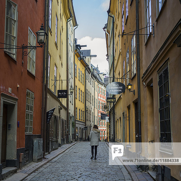Eine Frau geht eine Straße zwischen bunten Einzelhandels- und Wohngebäuden entlang; Stockholm  Schweden'.