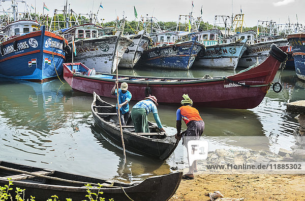 'Fishermen pushing small boat out and colourful fishing boats; Kadappuram  Kerala  India'