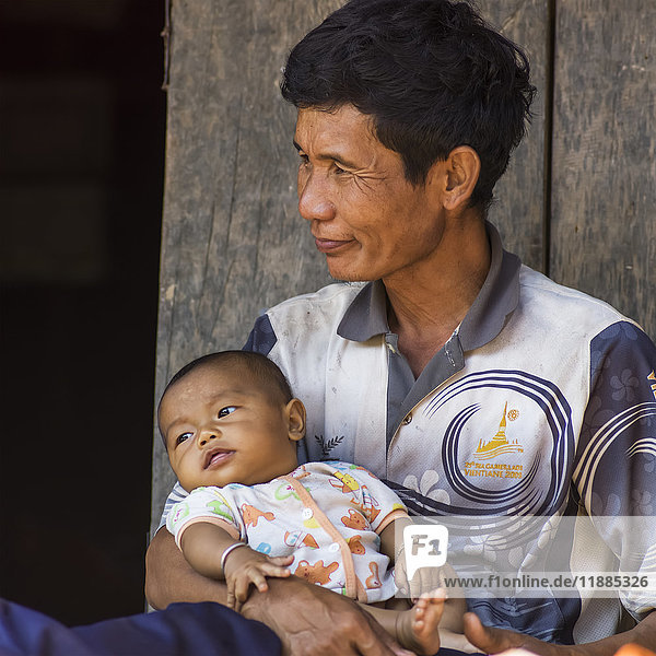 'A man sits smiling and holding his baby  Kamu village; Tambon Po  Chang Wat Chiang Rai  Thailand'
