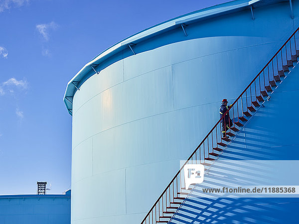 Ein Handwerker erklimmt die Treppe eines großen  blauen Lagertanks in einer Raffinerie; Edmonton  Alberta  Kanada .
