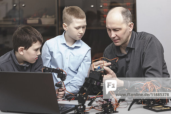 Neugierige Schülerinnen und Schüler  die den Lehrer beim Bedienen von Maschinen am Tisch beobachten.