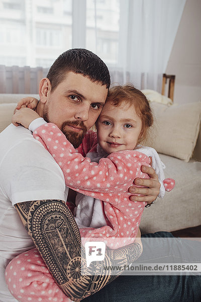 Porträt eines lächelnden Vaters und einer lächelnden Tochter  die sich auf dem Sofa zu Hause umarmen.