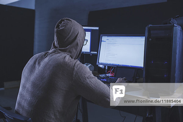 Computer hacker wearing hooded shirt using computer at table
