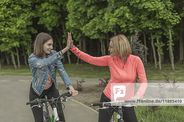 Lächelnde Mutter und Tochter  die beim Radfahren im Park high-five machen