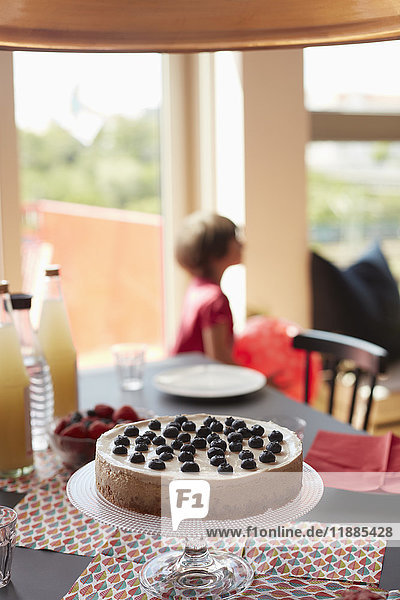 Torte auf Standmatten am Esstisch mit spielendem Mädchen im Hintergrund