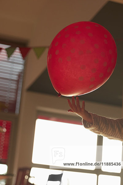 Abgeschnittenes Bild vom Spielen der Hand mit dem roten Ballon im Raum zu Hause