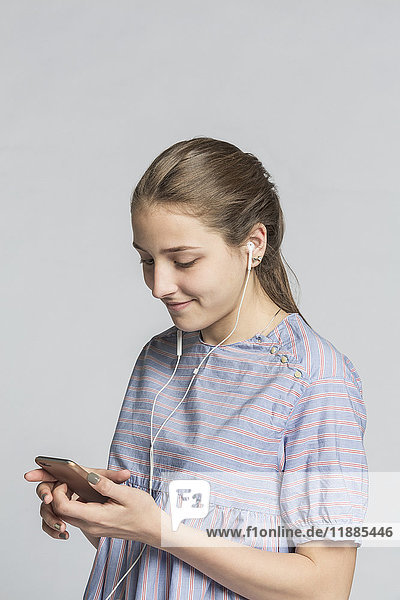 Smiling girl listening to music while using mobile phone against white background
