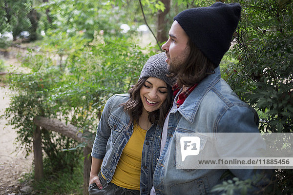 Affectionate couple wearing denim jackets and knit hats at park