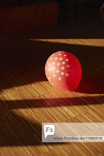 Hochwinkelansicht des gefleckten roten Ballons auf Hartholzboden im Sonnenlicht zu Hause