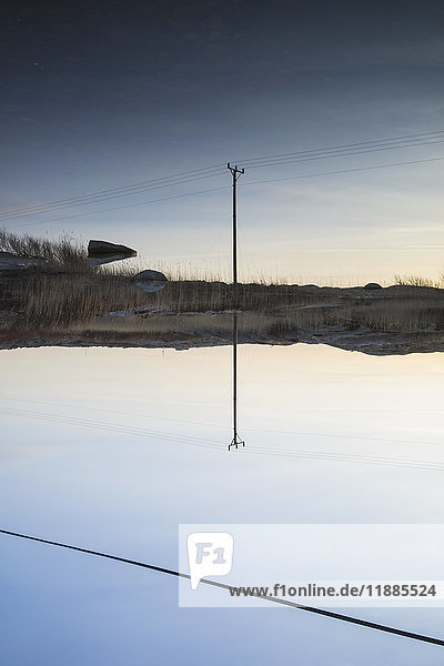 Strommast reflektiert im ruhigen See gegen den blauen Himmel