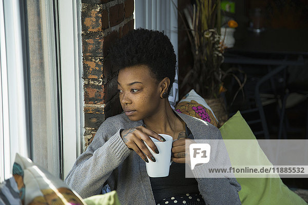 Junge Frau mit Kaffee und Blick durchs Fenster zu Hause