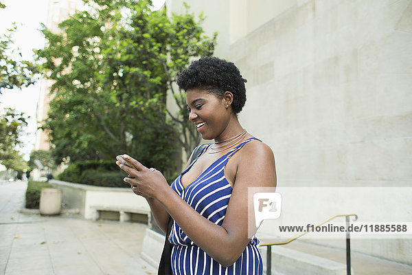 Side view of smiling woman text messaging through mobile phone against buildings in city