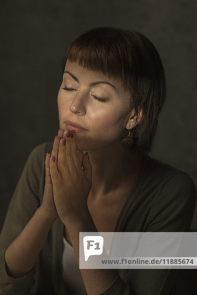 Mid adult woman with closed eyes praying against gray background