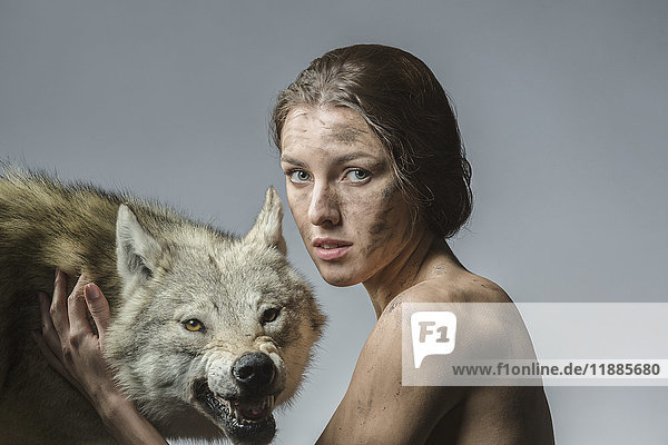 Porträt einer schmutzigen nackten Frau mit Wolf vor grauem Hintergrund