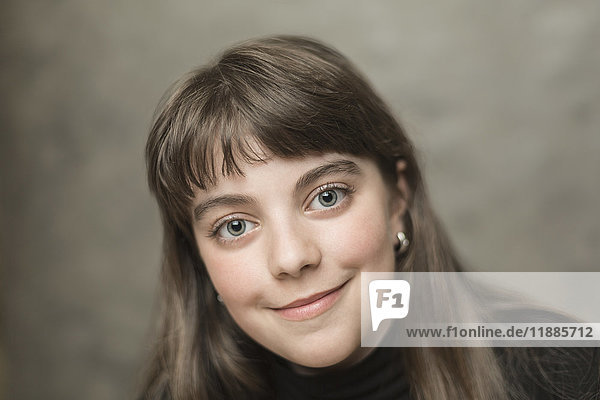 Porträt eines lächelnden Mädchens mit langen braunen Haaren vor grauem Hintergrund