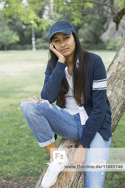 Portrait of young woman sitting on tree trunk at park