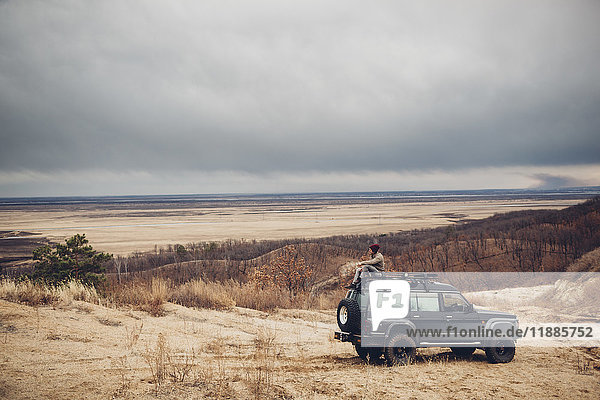 Distant man sitting on top of sports utility vehicle at field against cloudy sky  Amur  Russia