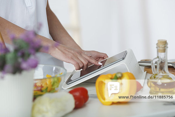 Cropped image of woman using digital tablet while preparing salad at kitchen counter
