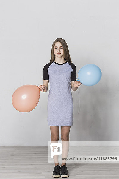 Portrait of teenage girl holding balloons standing against white wall