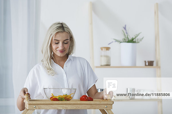 Schöne junge Frau hält Salatschüssel und Tomaten im Serviertablett in der Küche.
