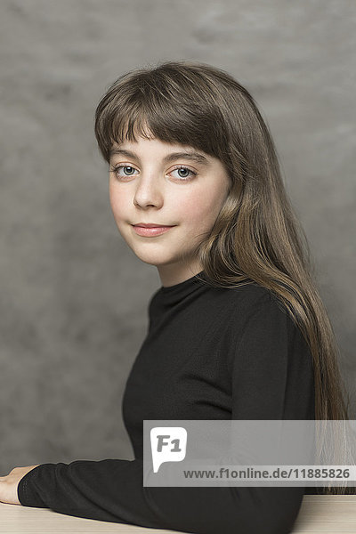 Porträt eines schönen lächelnden Mädchens mit langen Haaren am Tisch vor grauem Hintergrund