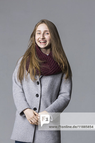 Portrait of cheerful teenage girl standing against gray background