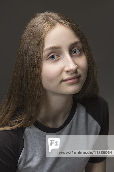 Close-up portrait of teenage girl with long brown hair against gray background