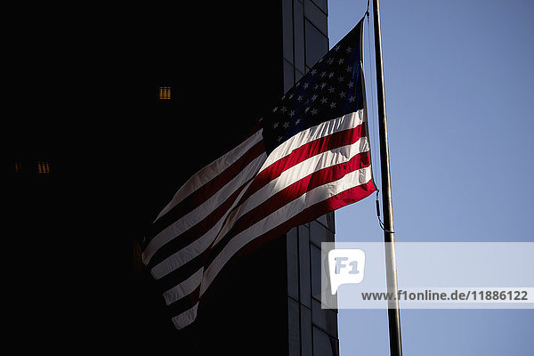Low angle of waving flag by building in city against clear sky