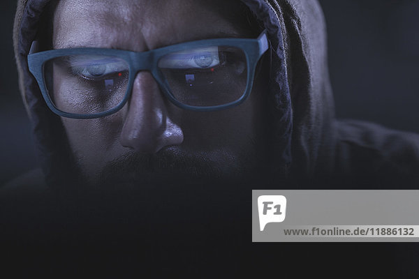 Close-up of serious computer hacker wearing eyeglasses and hood