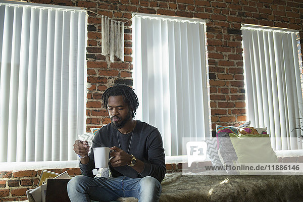 Mann auf dem Bett sitzend mit Kaffeetasse an den Fenstern zu Hause