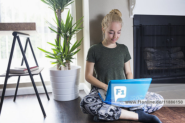 Young blond woman using laptop against wall at home