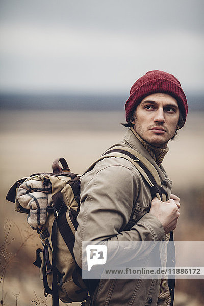 Thoughtful hiker carrying backpack and looking away while standing outdoors