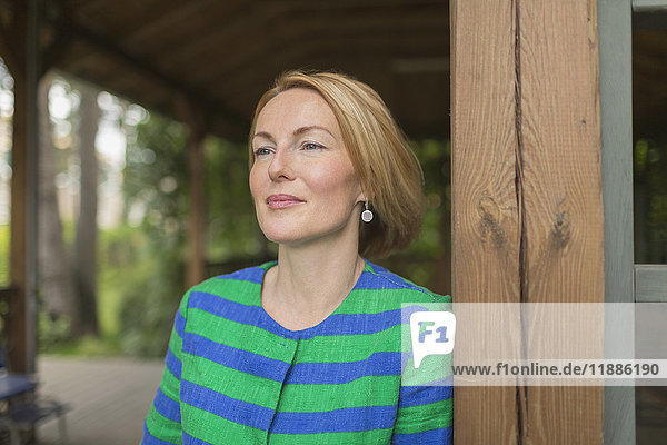 Nachdenkliche Frau  die sich auf eine Holzwand in einem Pavillon im Park stützt.