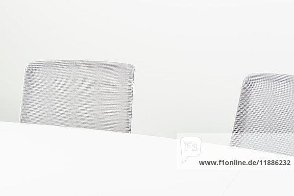 Hochwinkelansicht von grauen Bürostühlen mit Tisch vor weißem Hintergrund