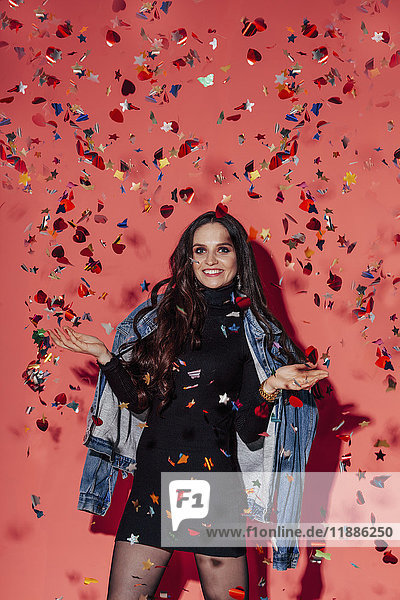 Portrait of happy young fashionable woman standing amidst confetti against coral background