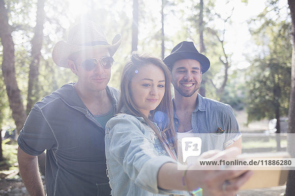 Schöne Frau nimmt Selfie mit männlichen Freunden durch Smartphone im Park während des sonnigen Tages.