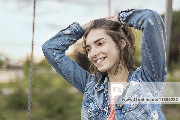 Lächelnde junge Frau mit der Hand im Haar  die in den Park schaut.