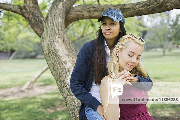 Young lesbian couple sitting against tree trunk at park