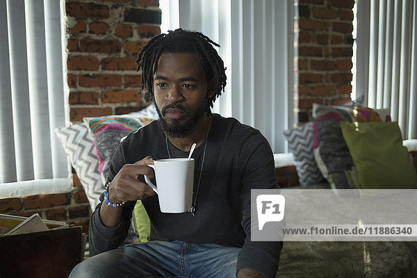 Nachdenklicher erwachsener Mann mit Kaffeetasse zu Hause sitzend