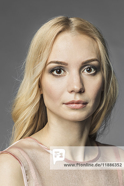 Porträt einer schönen jungen Frau mit blonden Haaren vor grauem Hintergrund