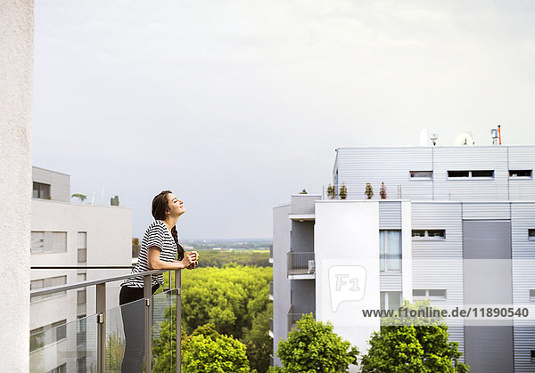 Frau mit Tasse Kaffee auf dem Balkon stehend