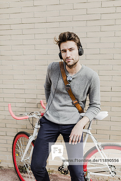 Portrait of young man with racing cycle and headphones