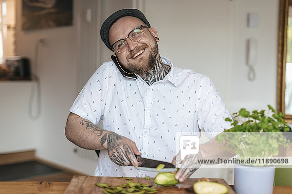 Lächelnder Mann am Telefon beim Gemüsehacken in der Küche